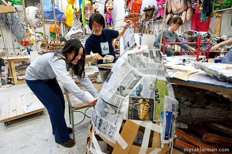 Marching towards FestiFools 2009 | Amanda Yu  and Shuli Qu (School of Public Health volunteers) affix news clippings of great economic and national security significance (“Dancing with the stars…”) to a cardboard puppet skeleton. Amy Sumerton (volunteer) takes a break from her day job as the Program Director at 826michigan to “do glue.” By the way, check out 826michigan’s special pre-Fools program: Robot-Costume-Building Workshop &amp; FestiFools Invasion!