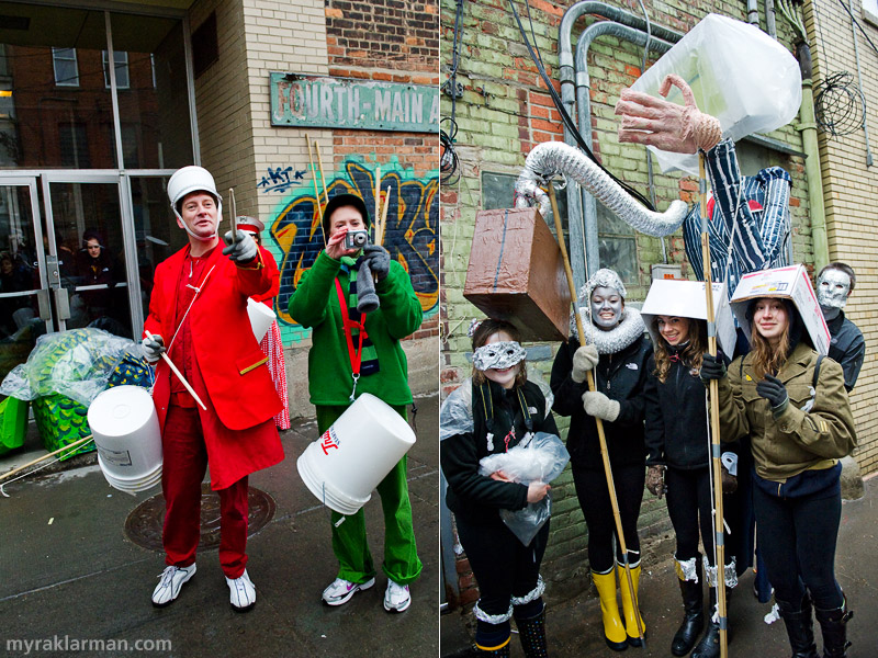 FestiFools 2011 | Puppets, their wranglers, and performers begin to line up in the alleys behind Main Street. Professor Nick Tobier (shown here modeling a très-sophisticated, bright-red suit, tastefully accessorized with an understated, 5-gallon plastic bucket) serves on the FestiFools steering committee; for the past several years, he’s had his U-M School of Art &amp; Design students create puppets and bring them to FestiFools as part of their coursework. | Plastic bags and cardboard boxes afford some protection from the driving rain. 