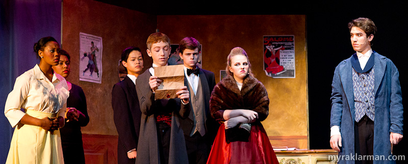 Pioneer Theatre Guild: Phantom of the Opera | The Phantom’s “Notes” are read aloud, with palpable disdain for their content. (l-r: Jassadi Moore, Lauren Victor, Jonathan Jue-Wong, Michael Shapiro, Jordan McKay, Clare Lauer, and Ari Axelrod)

